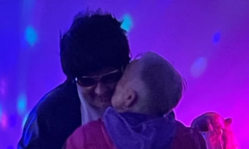 Bildet viser en eldre dame som gir en mann utkledd som Elvis, et lite kyss på kinnet. Mannen har mørke solbriller og en svart parykk på seg. Damen har kort, lyst hår.