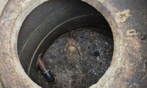 Øverste del av en slamavskiller sett ovenfra. Et rundt betongkammer med flere konsentriske ringer synlige innvendig. Bunnen av kammeret er dekket av mørkt slam. En liten del av et rør er synlig i nedre del av bildet.